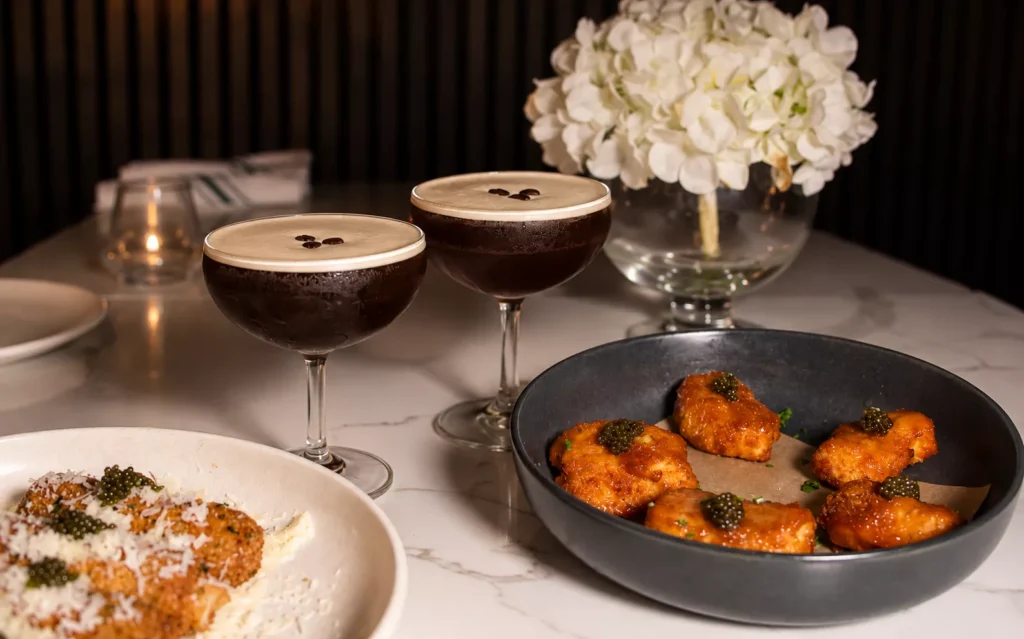 A dining table with two drinks and food at The Ainsworth