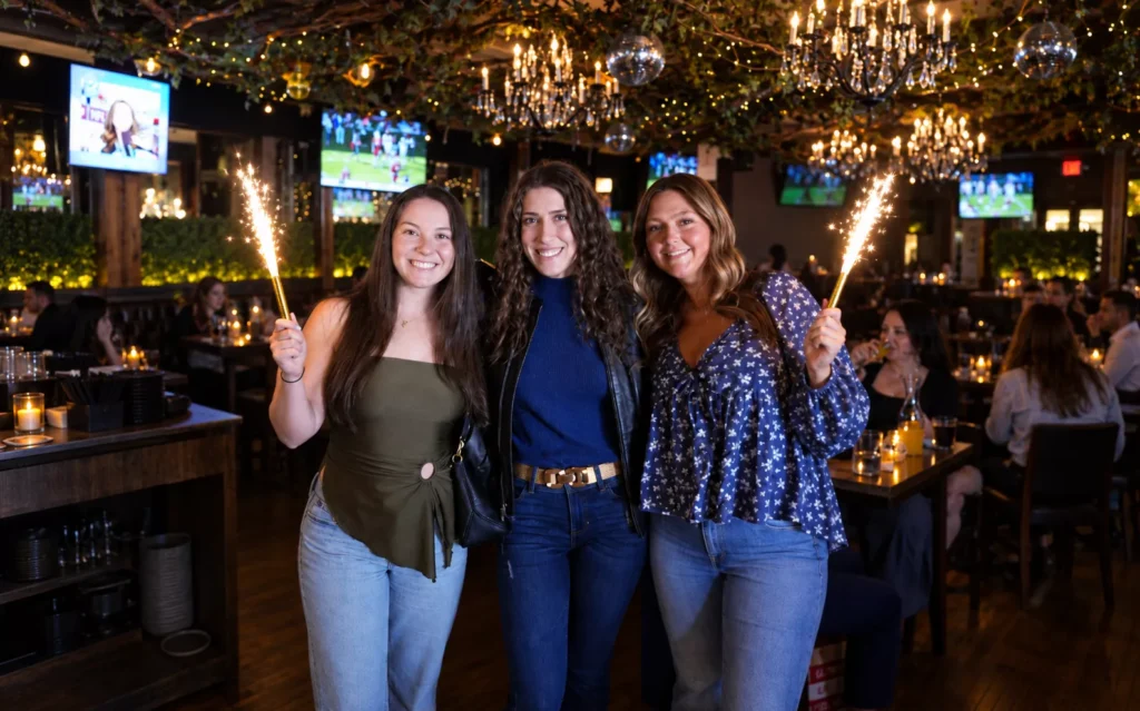 Three festive women with sparklers celebrating a birtday at the best restaurant for birtthday bases in Hoboken -- The Ainsworth 